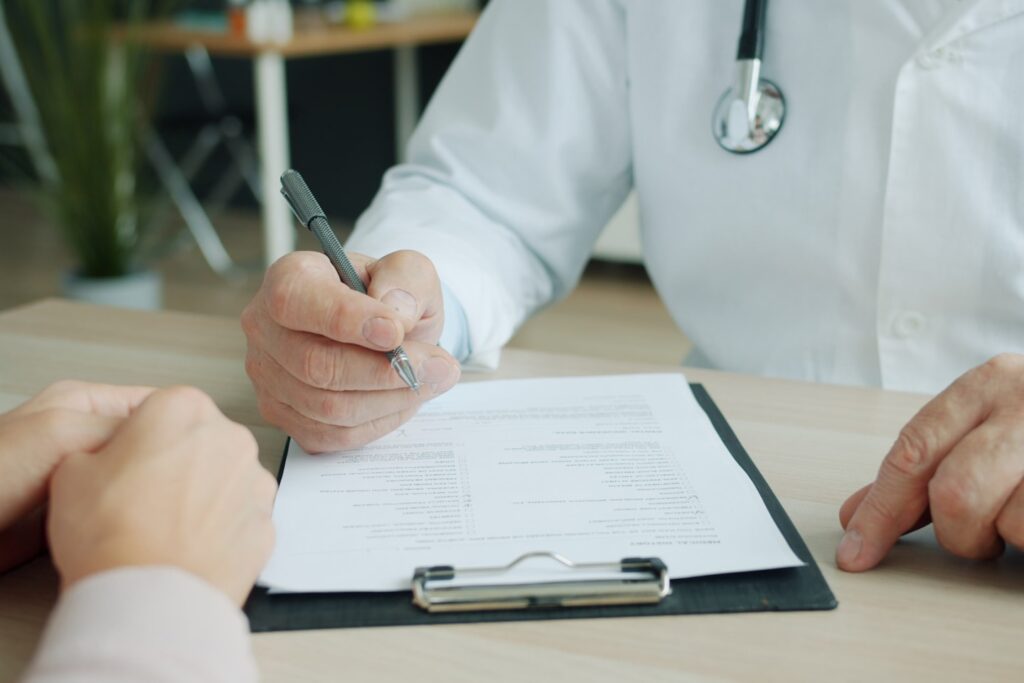 Medic in uniform is ticking symptoms in patient's medical records during appointment in clinic talking to patient sick woman. People and healthcare concept.